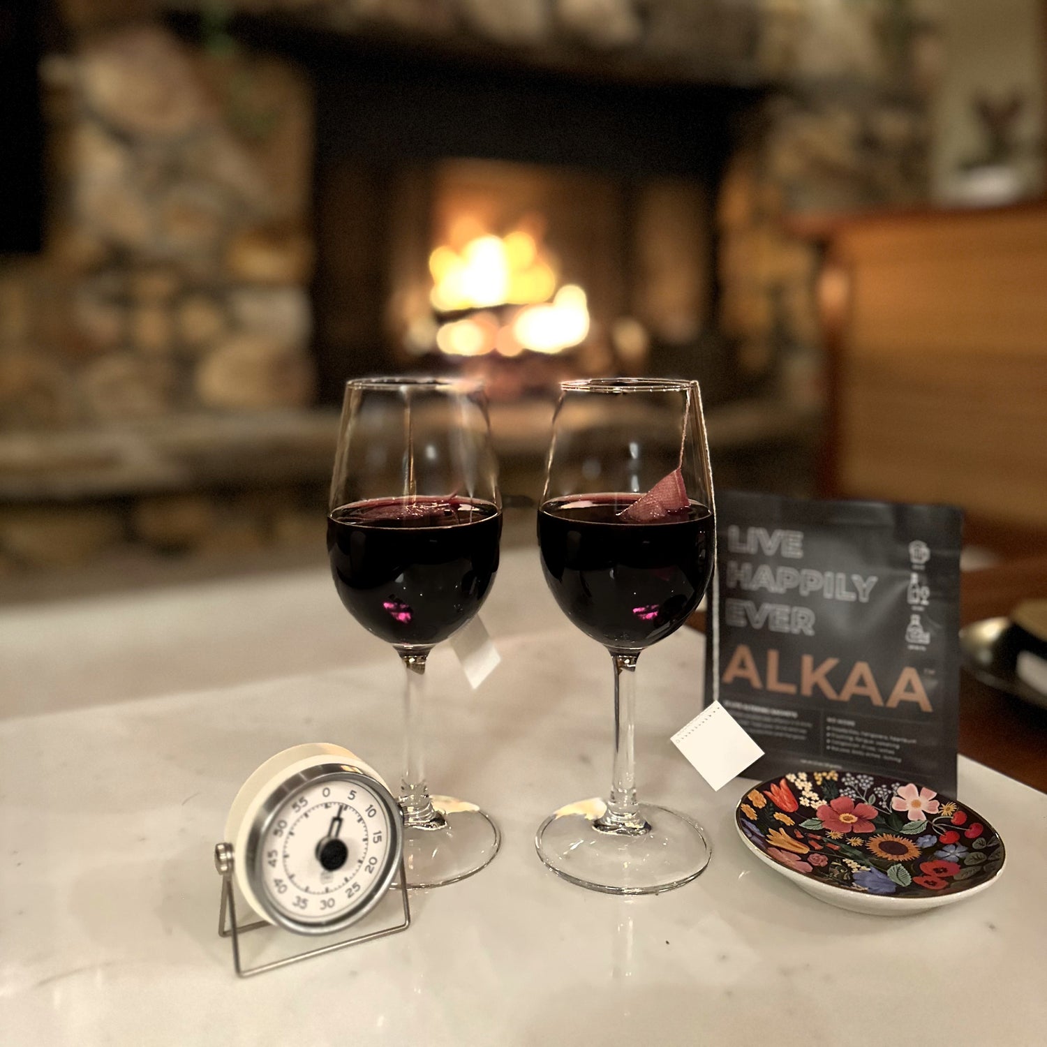 Two glasses of wine in front of a fire place where they ALKAA sachets are removing the problematic elements in alcohol.